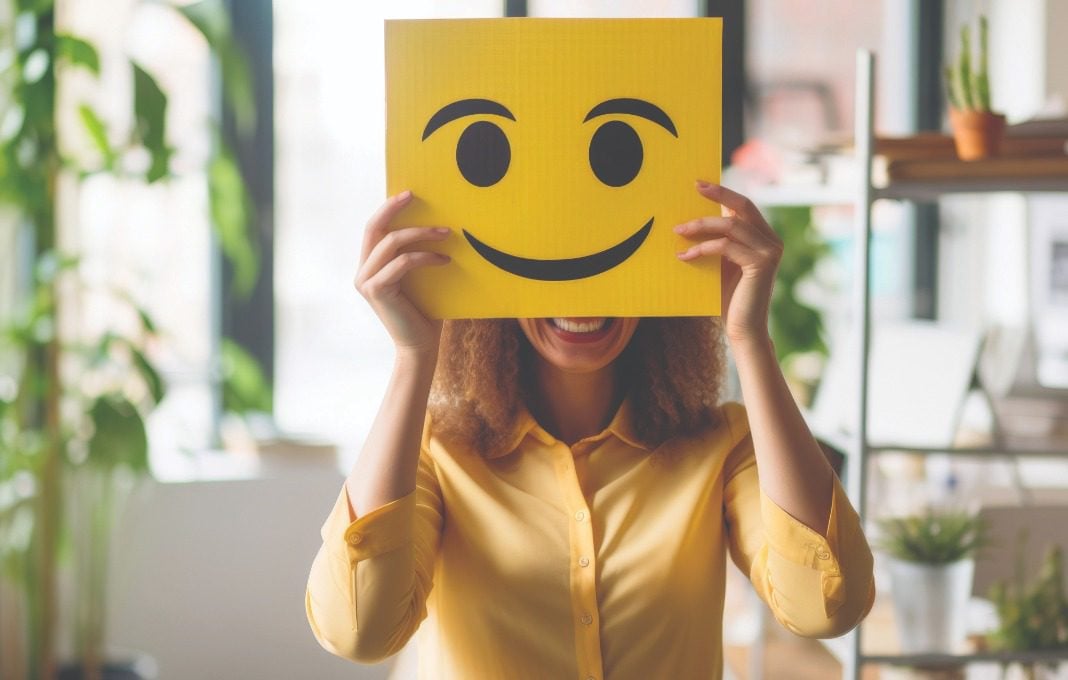 Woman holding drawn smiley face over her face