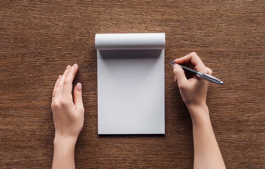 cropped view of person holding pen over blank notebook on wooden background