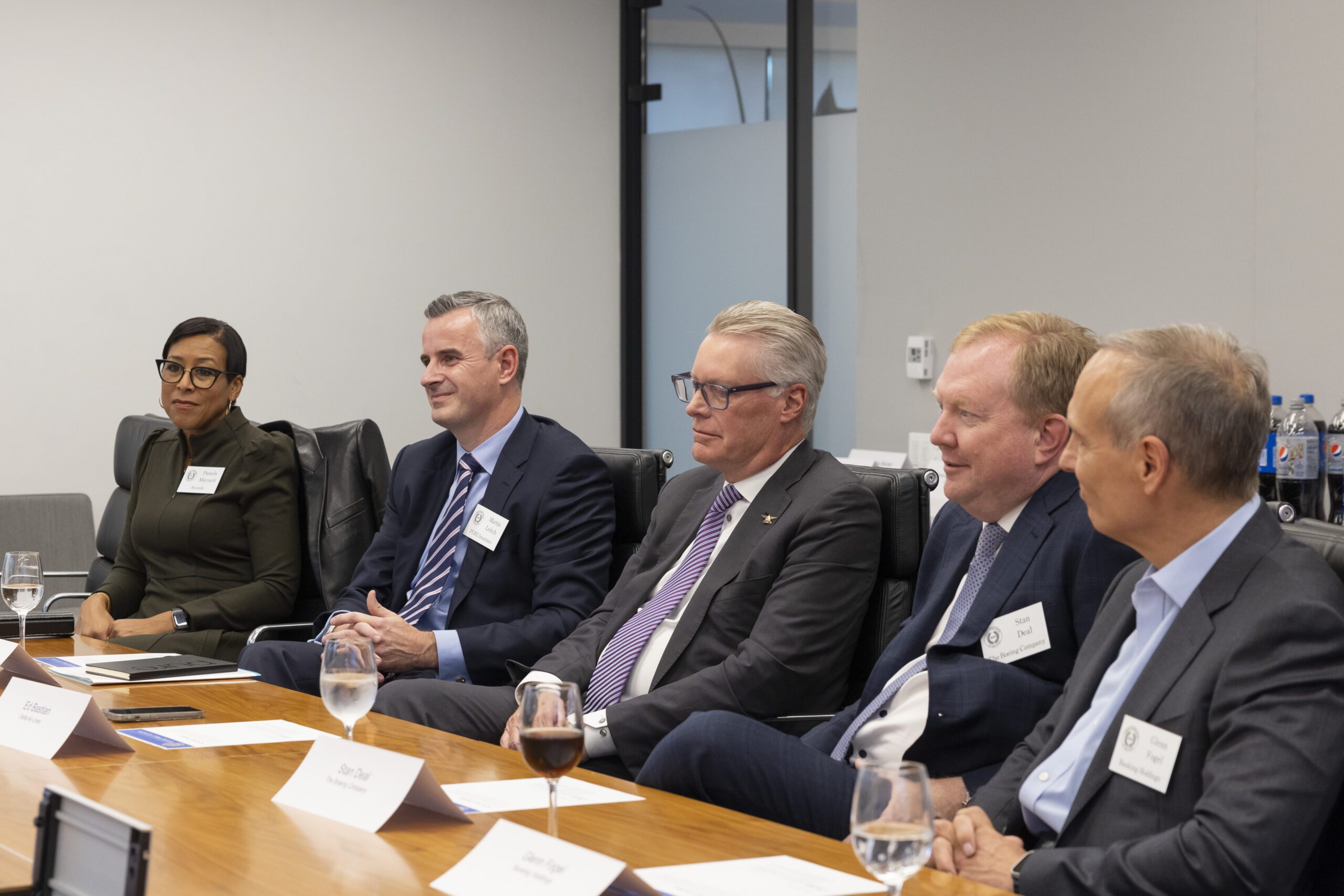A group of business executives seated at a board table having a discussion. Ed Bastian is seated in the middle.